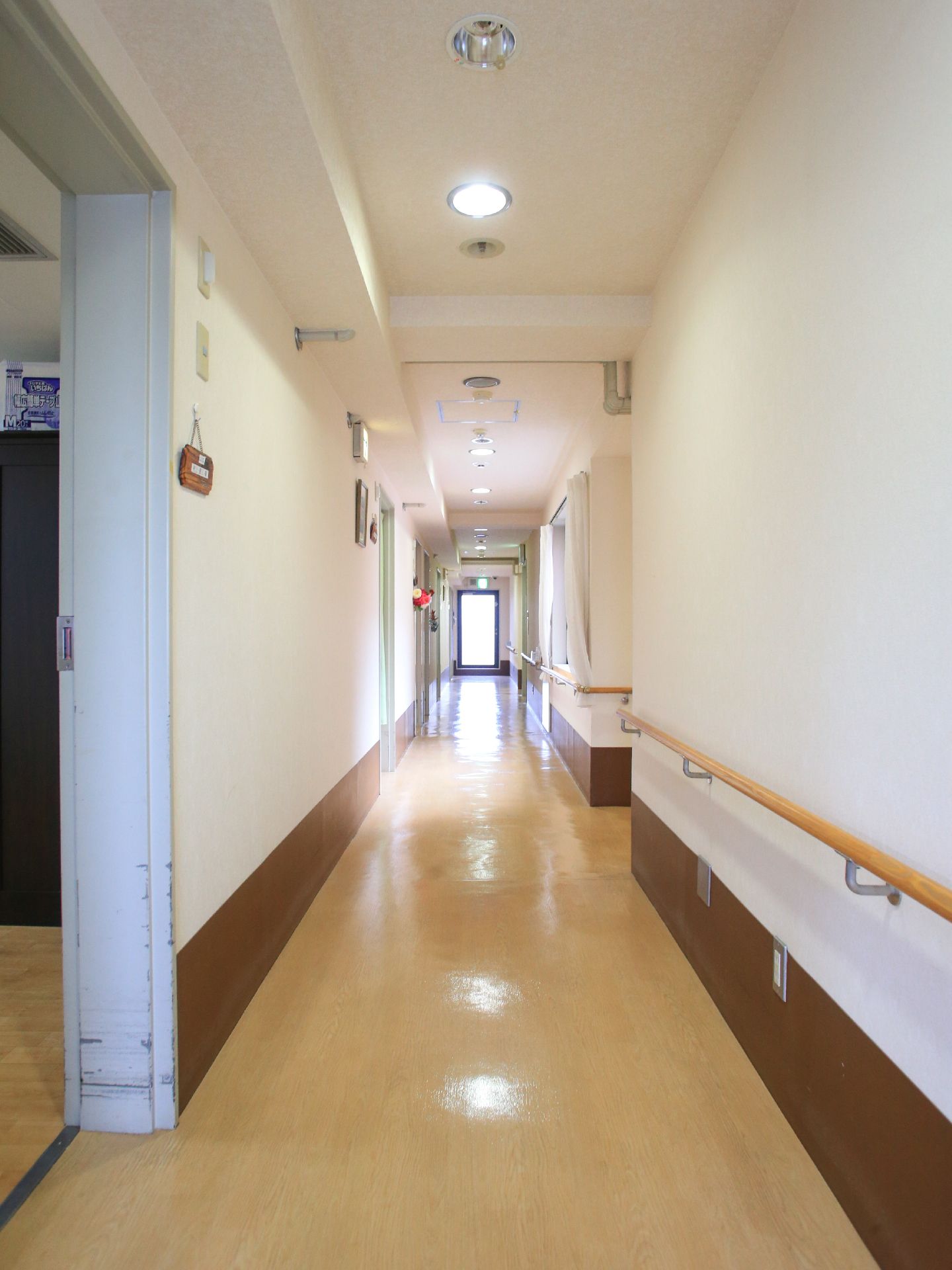 廊下の突き当たりからは明るい光が差し込んでおり右手の壁には曲がり角まで手すりが設置されており床はフローリングになっている。