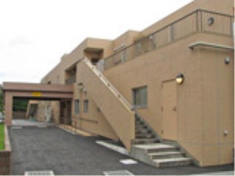 施設はベージュのしっかりした建物。玄関前には大きくせり出したひさしがあり、脇には手すりのついたスロープがある。