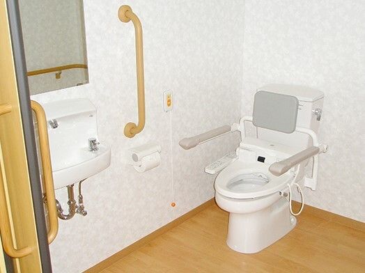 白を基調としたシンプルなトイレ。要所に手すりが取り付けられている。清掃用具が充実しており、いつでも清潔に利用できる。