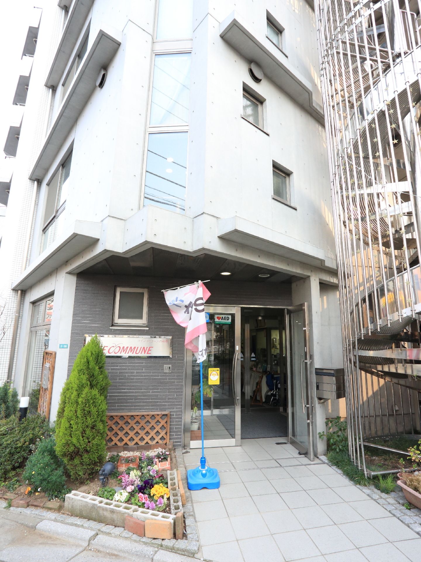コンクリート製のマンションのようなつくりの建物になっている。螺旋階段が右手にあり左側には花壇が手入れされている。
