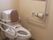 温水洗浄機能付きの洋式トイレである。後ろには背もたれが付いており、両サイドには手すりが設置されている。