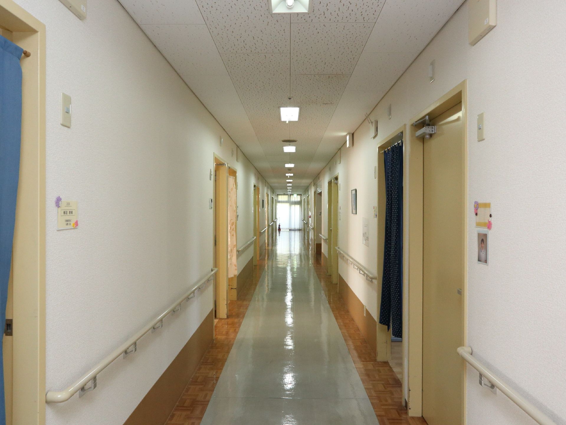 長い廊下がのびており突き当たりからは光がもれている。両側の壁には手すりが敷設され扉もところどころに見える。