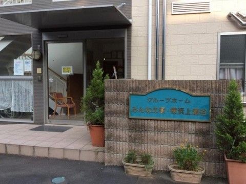 正面には本施設名が書かれた青いプレートがはめ込まれている。玄関には多くの観葉植物を置いているので、安らげる雰囲気がある。