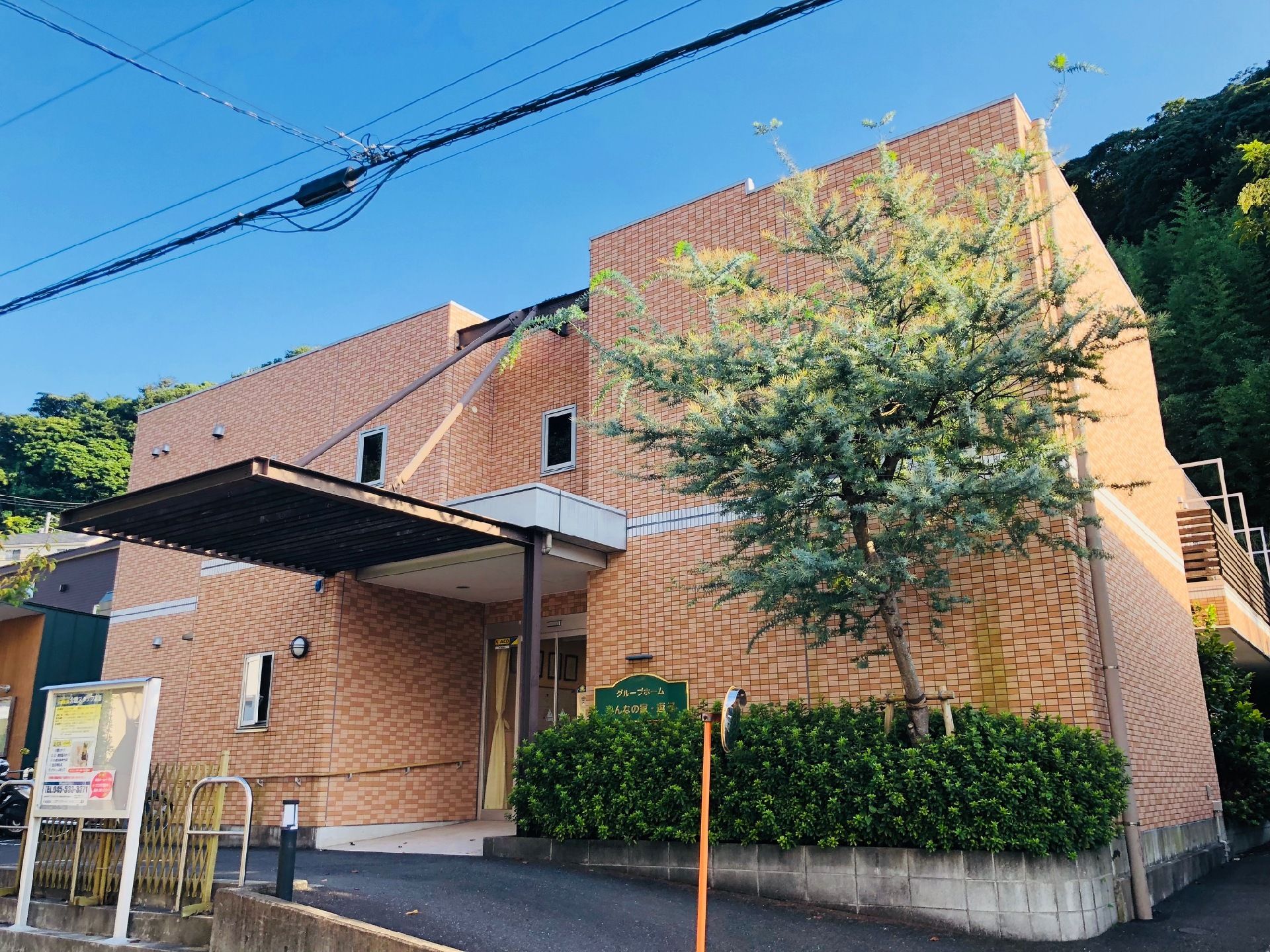 エントランスには大きな屋根が設けられているので、雨の日の送迎の際なども快適である。入り口横の外壁には施設名のプレートが掲げられている。