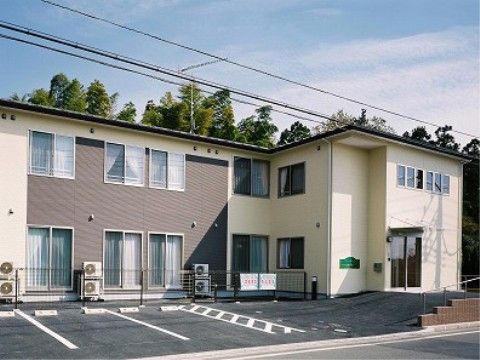 白とグレーを基調とした二階建ての施設。玄関前に段差がないため、車椅子をご利用の方でも安全に出入りすることができる。