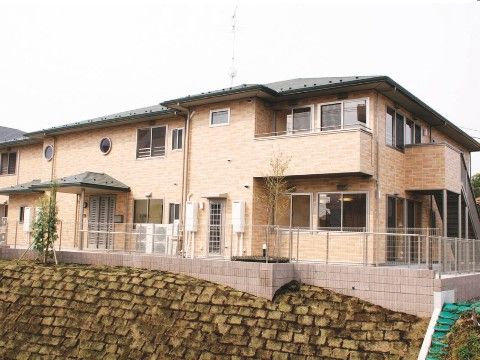 三角屋根の２階建ての施設は、高台に佇む日当たりの良い立地である。周りに格子のフェンスを設置している。