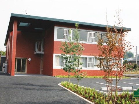 敷地内に植栽があり、玄関前に大きな庇がついた2階建ての建物