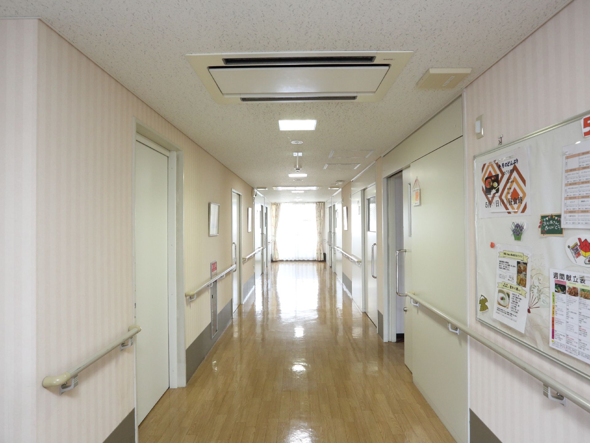 廊下の突き当たりからは光が差し込んでいる。天井に空調が取り付けられており壁面には手すりも敷設されている。