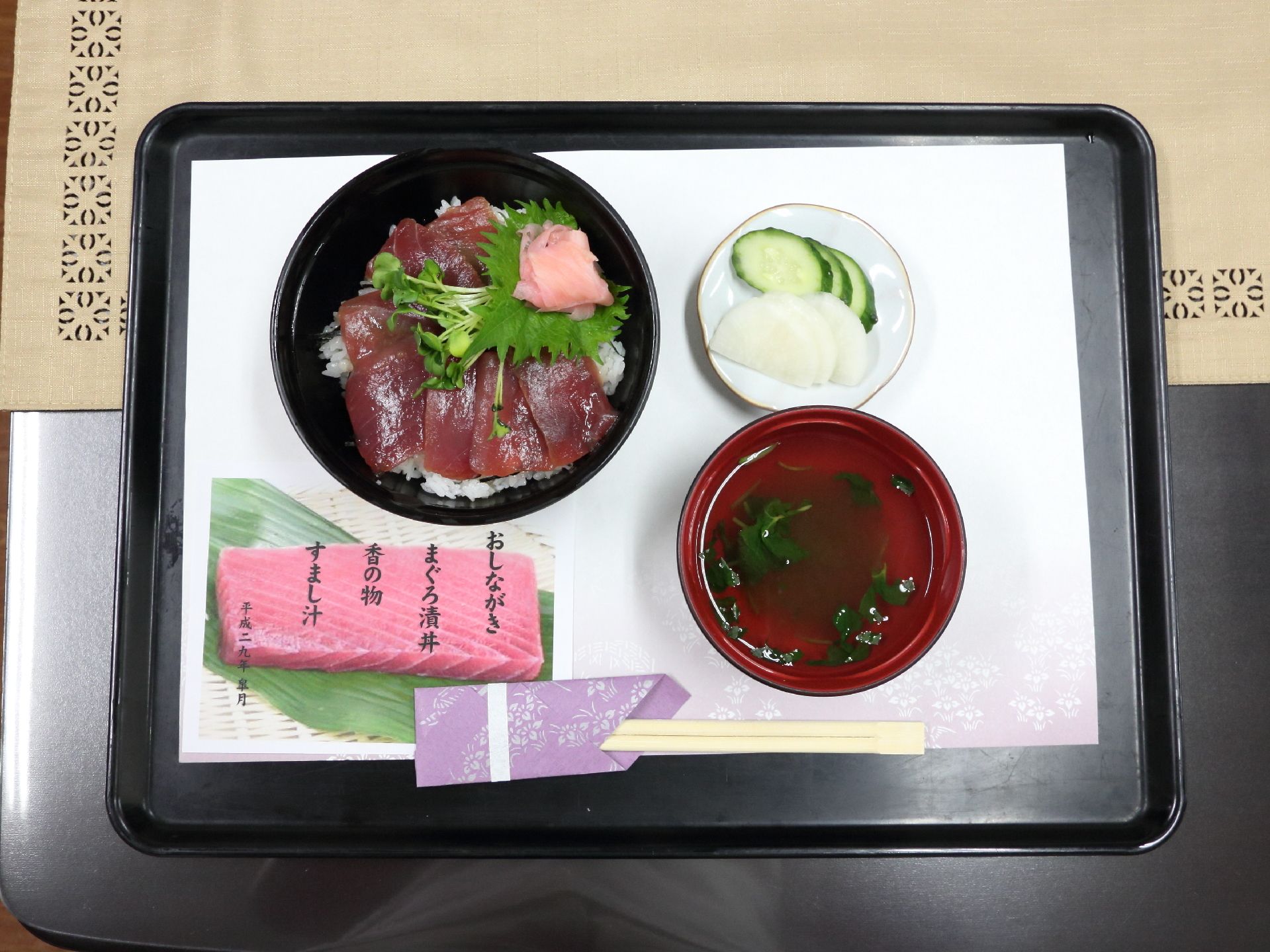 トレイの上におしながきと一緒に食事がのせられている。まぐろ漬け丼にすまし汁に香の物といった純和風の食事が提供されている。
