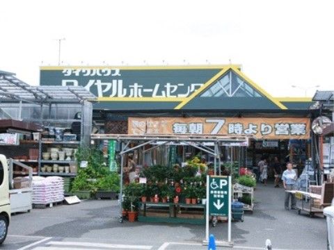 地域にあるホームセンターの入り口周辺の外観である。屋外に鉢植えなどの商品が並べられ、屋根の上の看板には店名が表示されている。