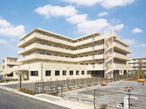 目の前に駐車場と公園があり、らせん状の非常階段がついた白い建物