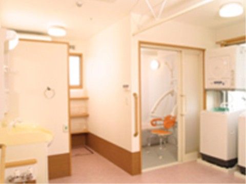 広い脱衣所である。洗濯機や乾燥機、洗面台が備え付けられている。壁にはタオルハンガーやナースコールが設置されている。
