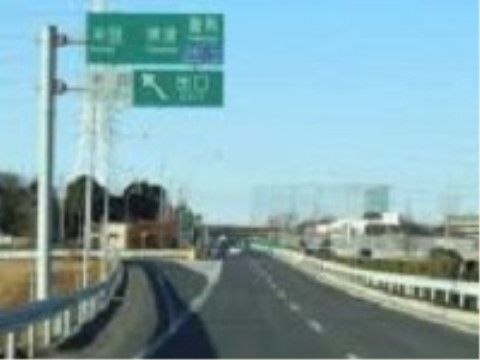 高速道路の写真である。緑色の道路標識が立てられており、両サイドには白いガードレールが設置されている。