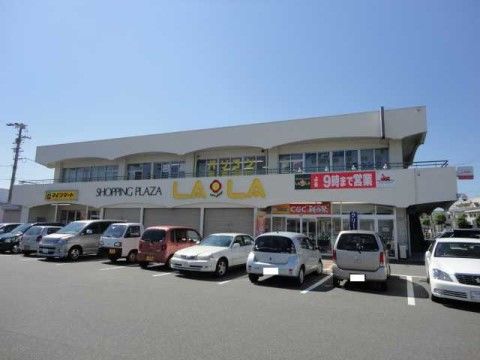 ２階建てのショッピングセンターの写真。白を基調とした外壁で、施設内にアスファルトで舗装された駐車場を設けている。