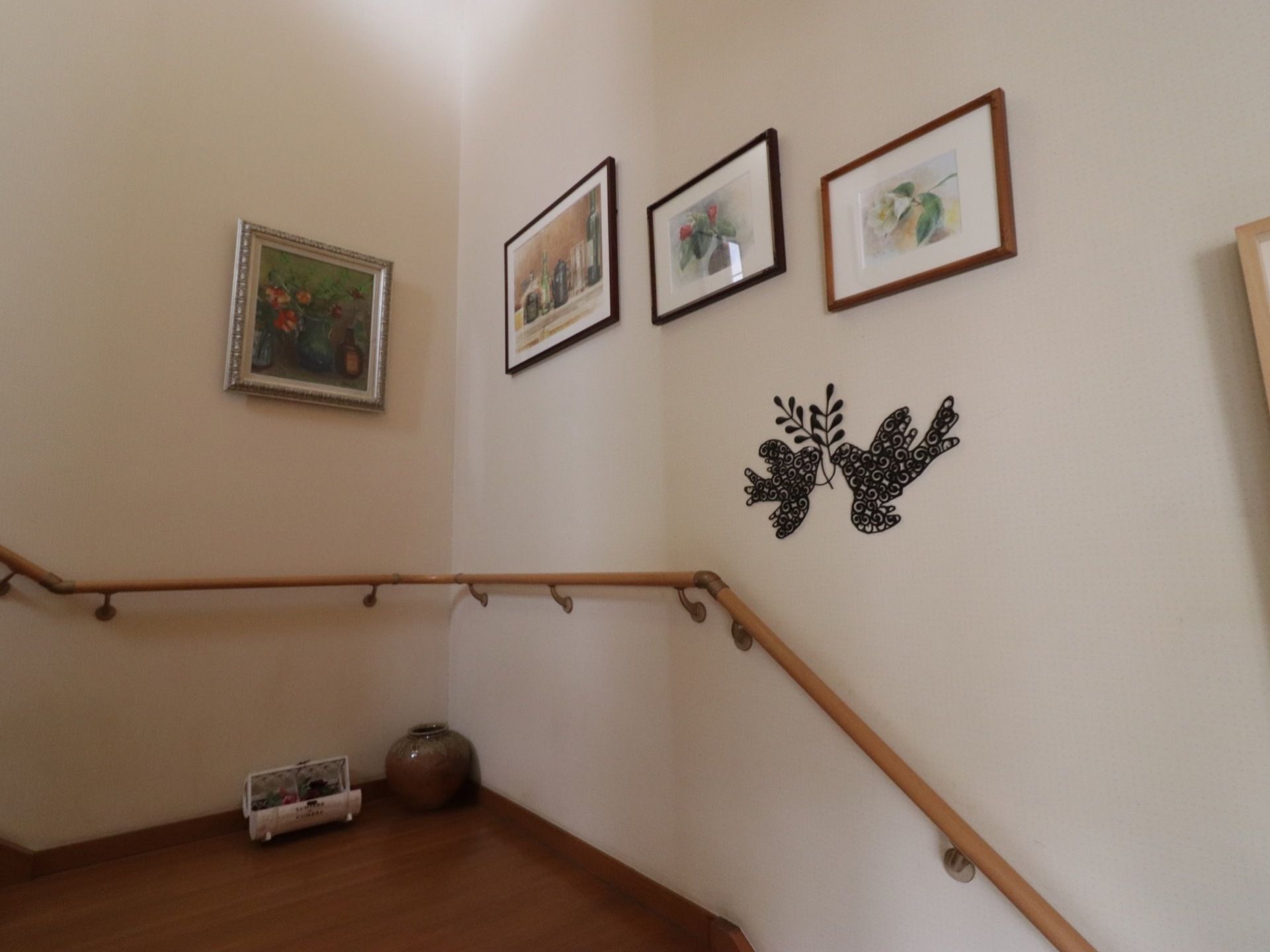 階段には手すりが設置されている。床はフローリングである。壁には絵画が飾られている。踊り場には焼き物、花が置かれている。