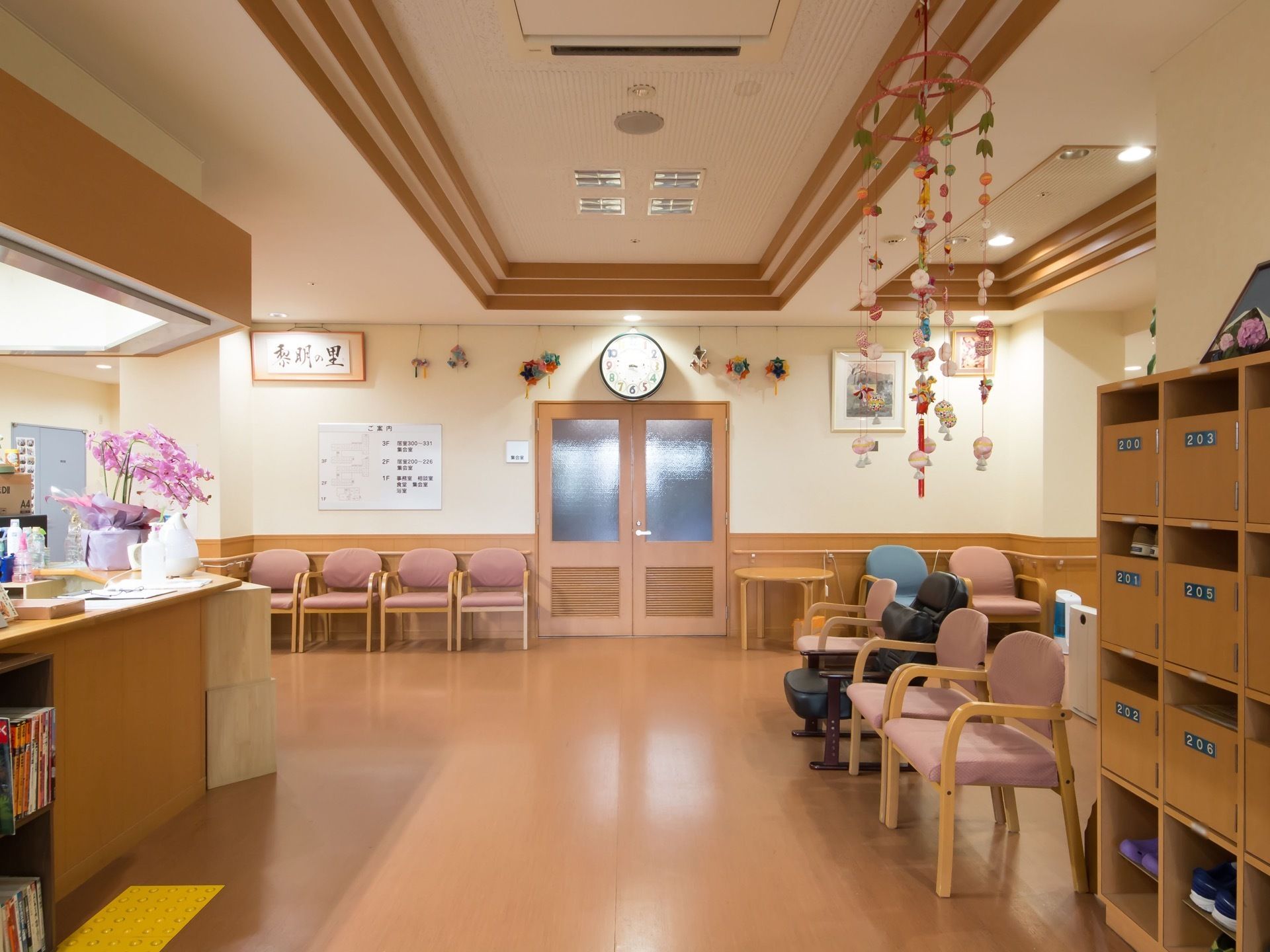 エントランスには大型の下駄箱が右手にある。壁際に１人用の椅子が並べられている。天井から吊るし雛が下げられている。