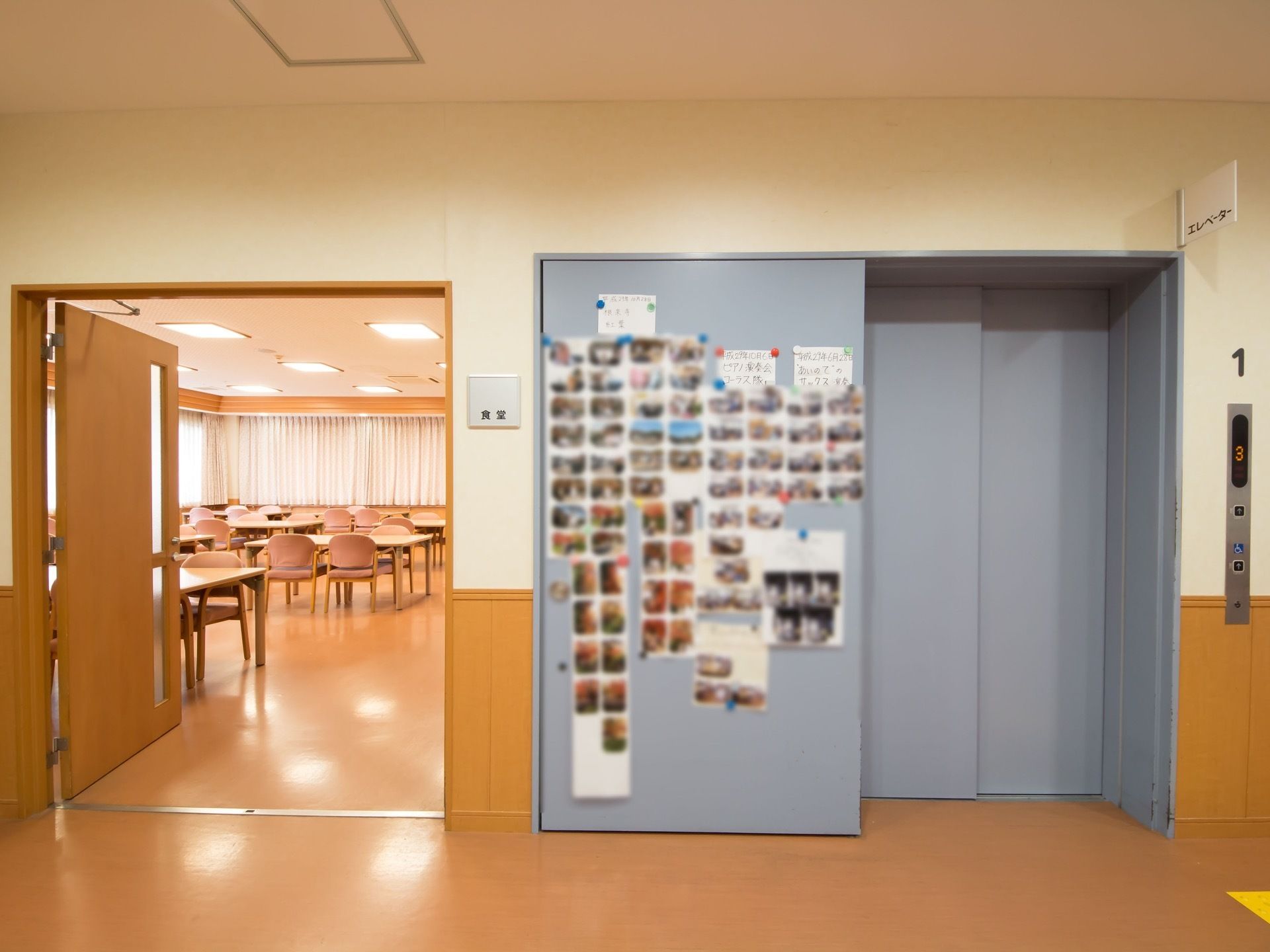 エレベーターの扉の横に、入居者様のスナップ写真などが貼られている。その横は共有スペースへの入口になっている。