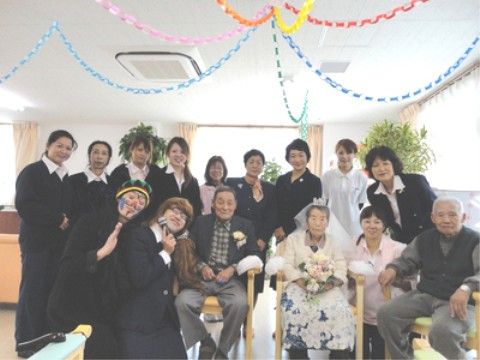 天井から紙飾りが垂れ下がる部屋で、笑顔で集合写真を撮影する入所者とスタッフ