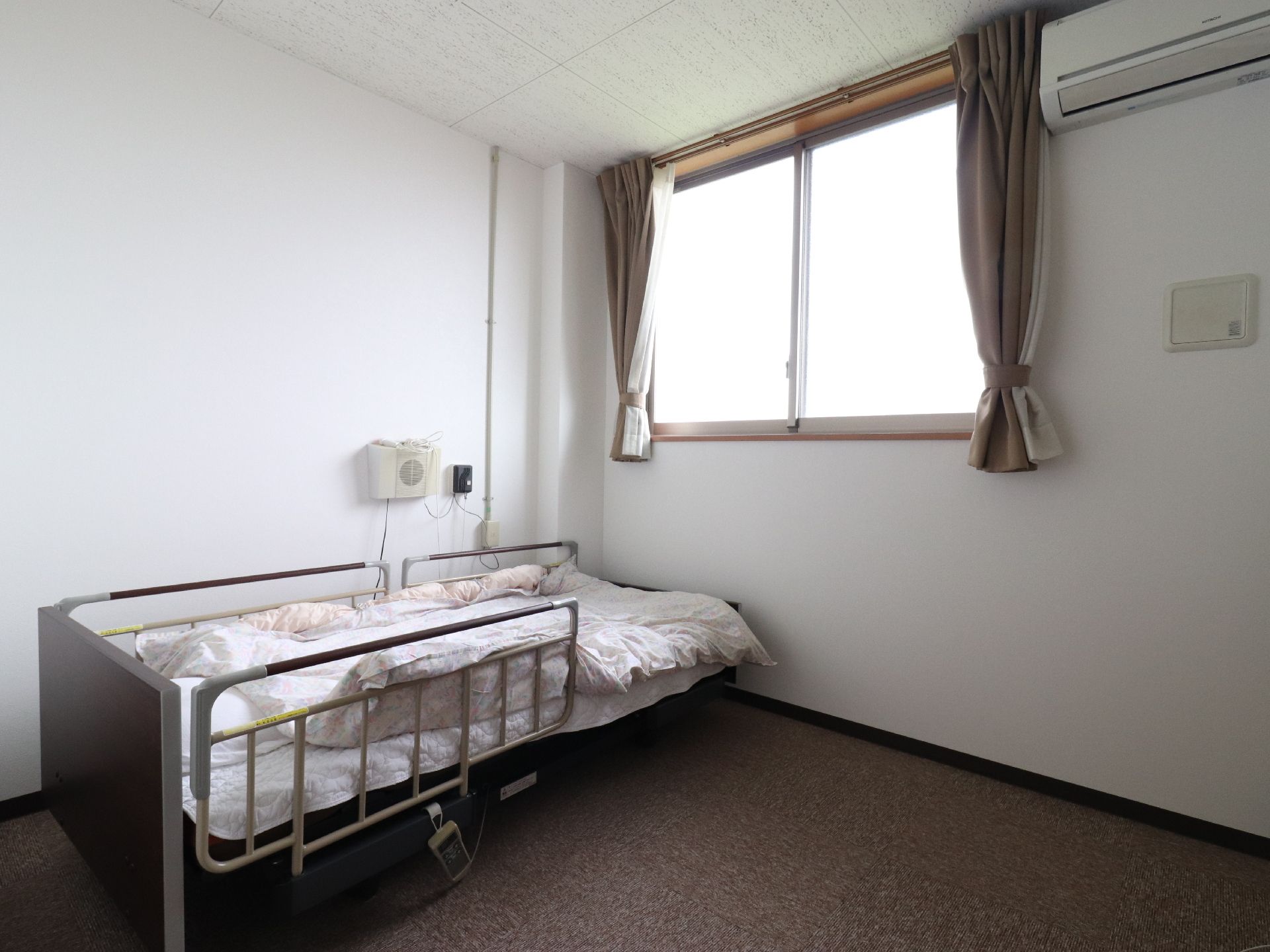柵つきの電動ベッドが置かれた、白い壁で腰の高さの窓がある部屋