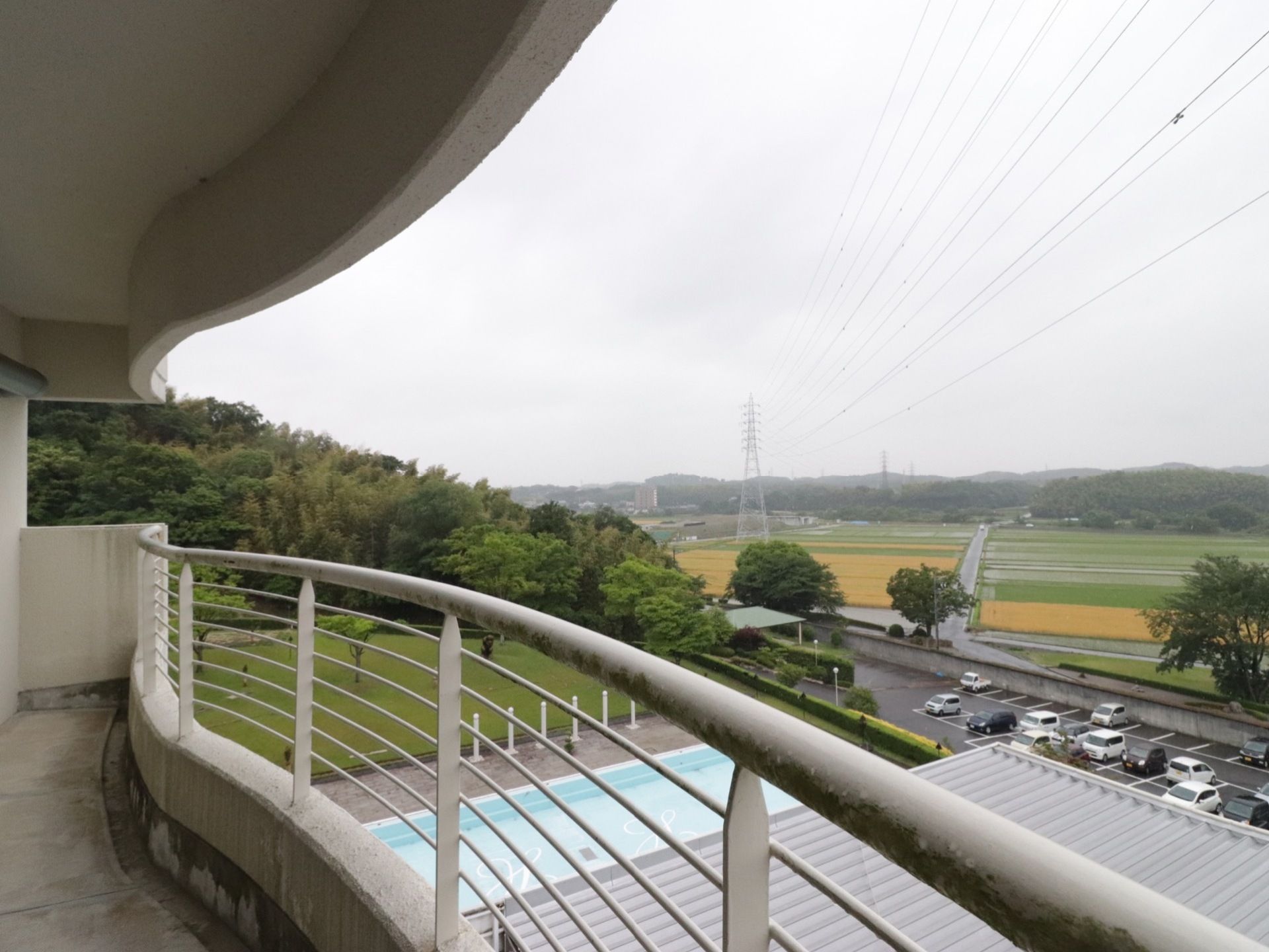 白い柵の取り付けられた、広やかなベランダである。下の方には、施設の野外プールや、駐車場を見ることができる。