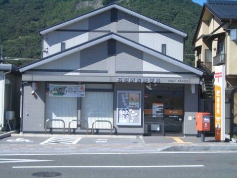 グレーの外壁がシックな２階建ての建物。駐車スペースが２台分確保されている。郵便、貯金、保険の取り扱いの他にATMが利用できる。