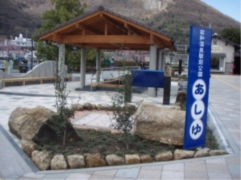 最寄り駅の目の前にある公園では足湯が無料で楽しめる。のぼりがたっており、奥に見えるあずま屋で足湯が利用できるようになっている。