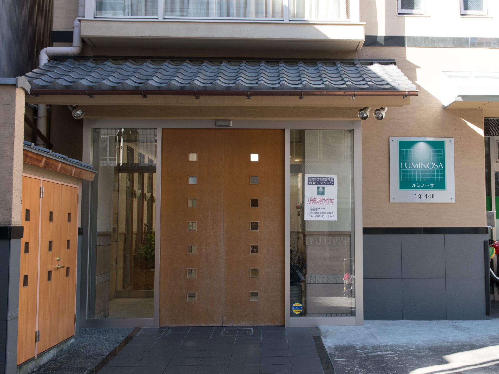 ルミノーサ三条小川の1階に併設されているデイサービスの入り口。木目調に小さいガラスがはめ込まれたおしゃれな雰囲気。