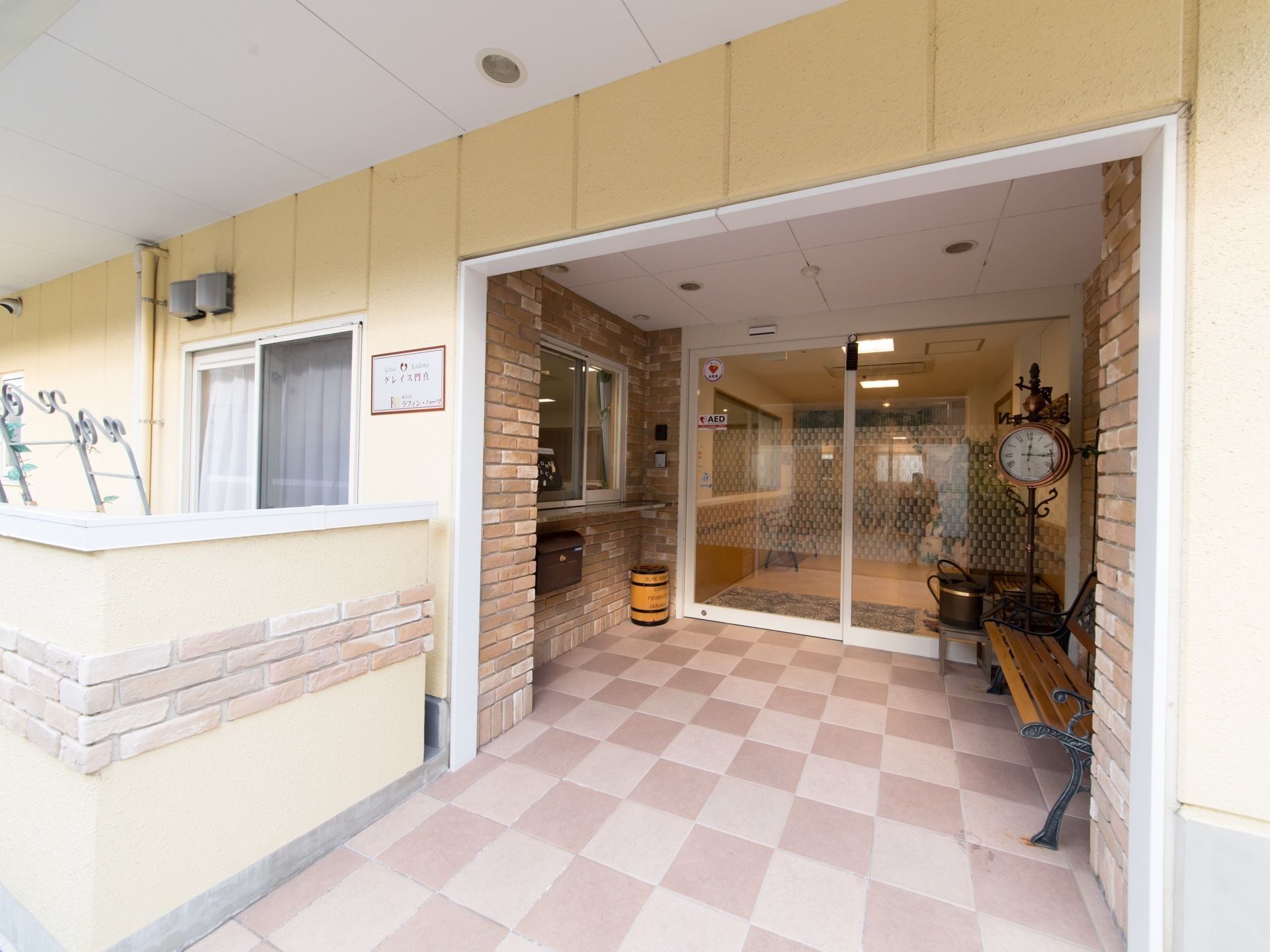 玄関前のアプローチは広々としたレンガ敷になっており、ベンチが置かれている。入り口の脇には受付が設けられている。