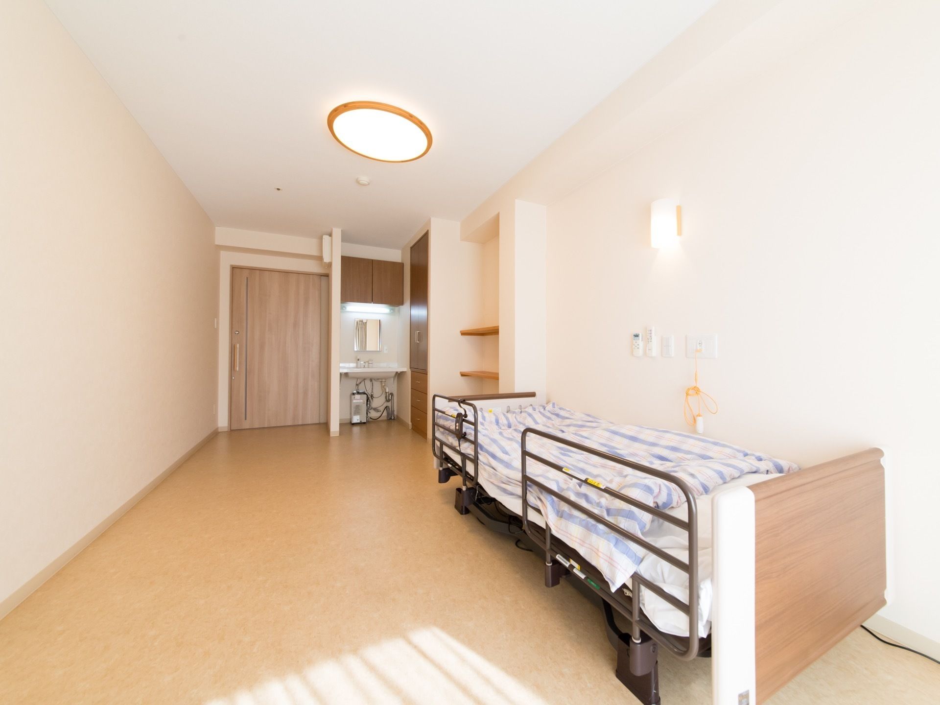 広々とした居室の壁際にベッドが置かれている。収納力がたっぷりとある、クローゼットタイプの収納スペースが設置されている。