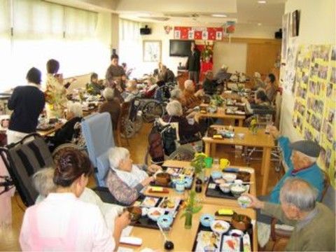 ダイニングテーブルに並ぶお膳を、みんなで並んで食べている入居者たち