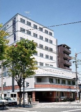 大きな植樹がある大通りに面した角地に建つ、玄関に大きな庇が付いた建物