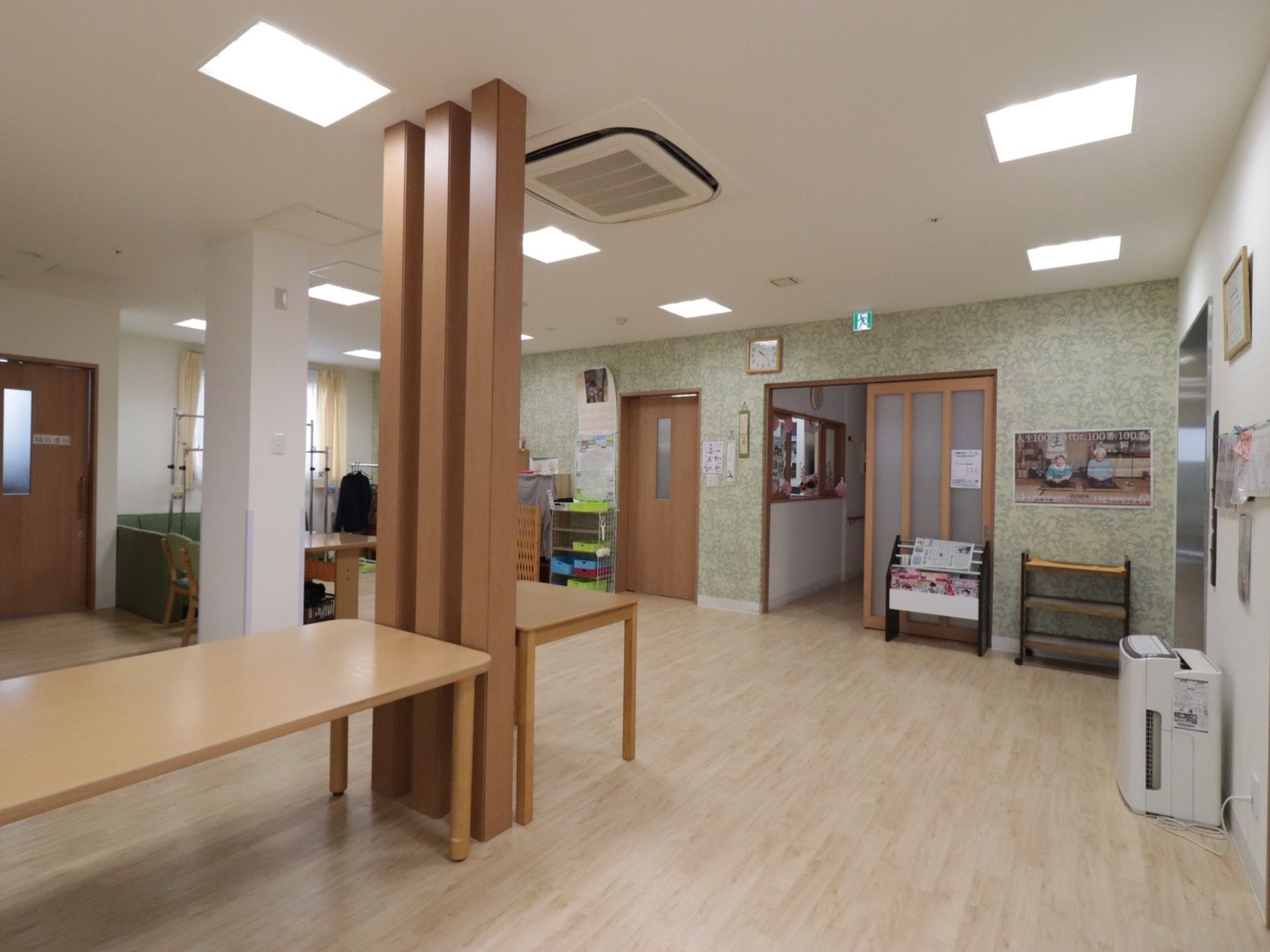 空調設備が整った共有スペースである。テーブルや椅子、ソファーが配備されている。壁には記念写真が貼られ、新聞や本が本立てに収められている。