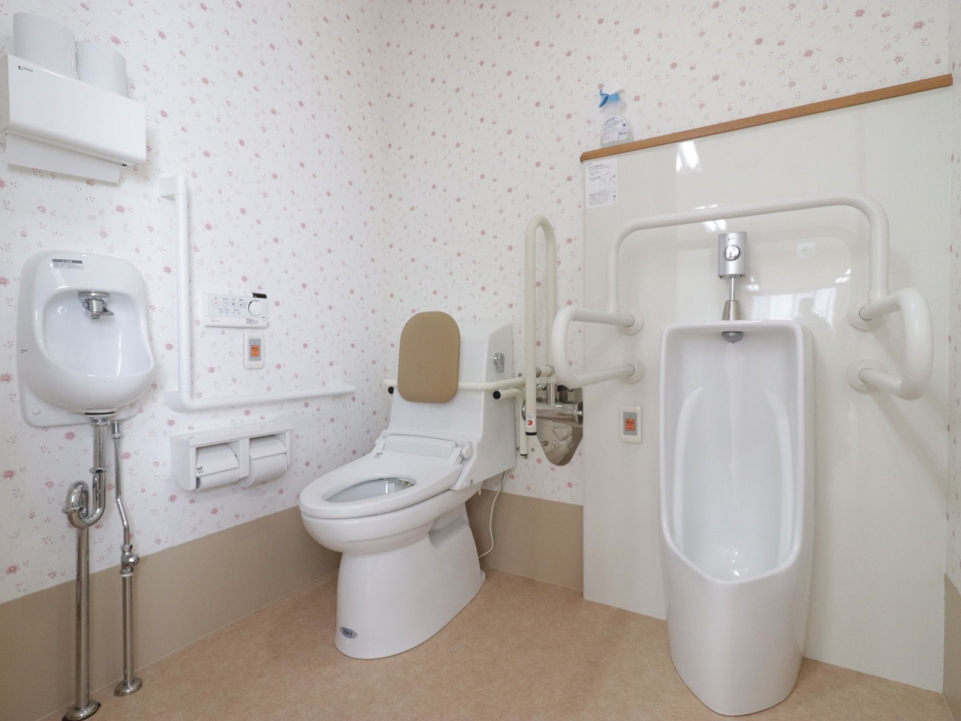 洋式便器と男性用便器と洗面台が設置されている。壁の各所に手すりがつけられている。模様のついた壁紙を使用している。