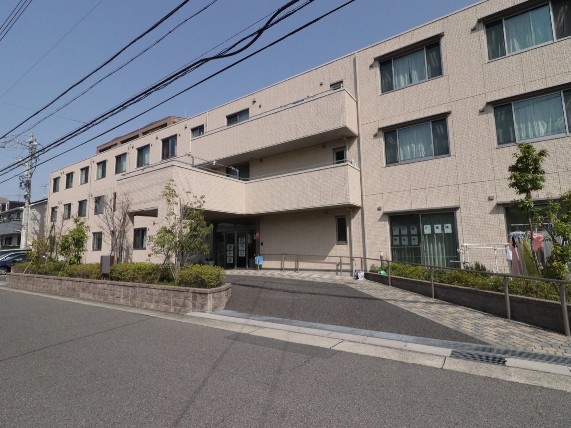 建物の前は駐車スペースになっていて、植栽スペースにたくさんの樹木が植えられている。スロープには手すりが設置されている。