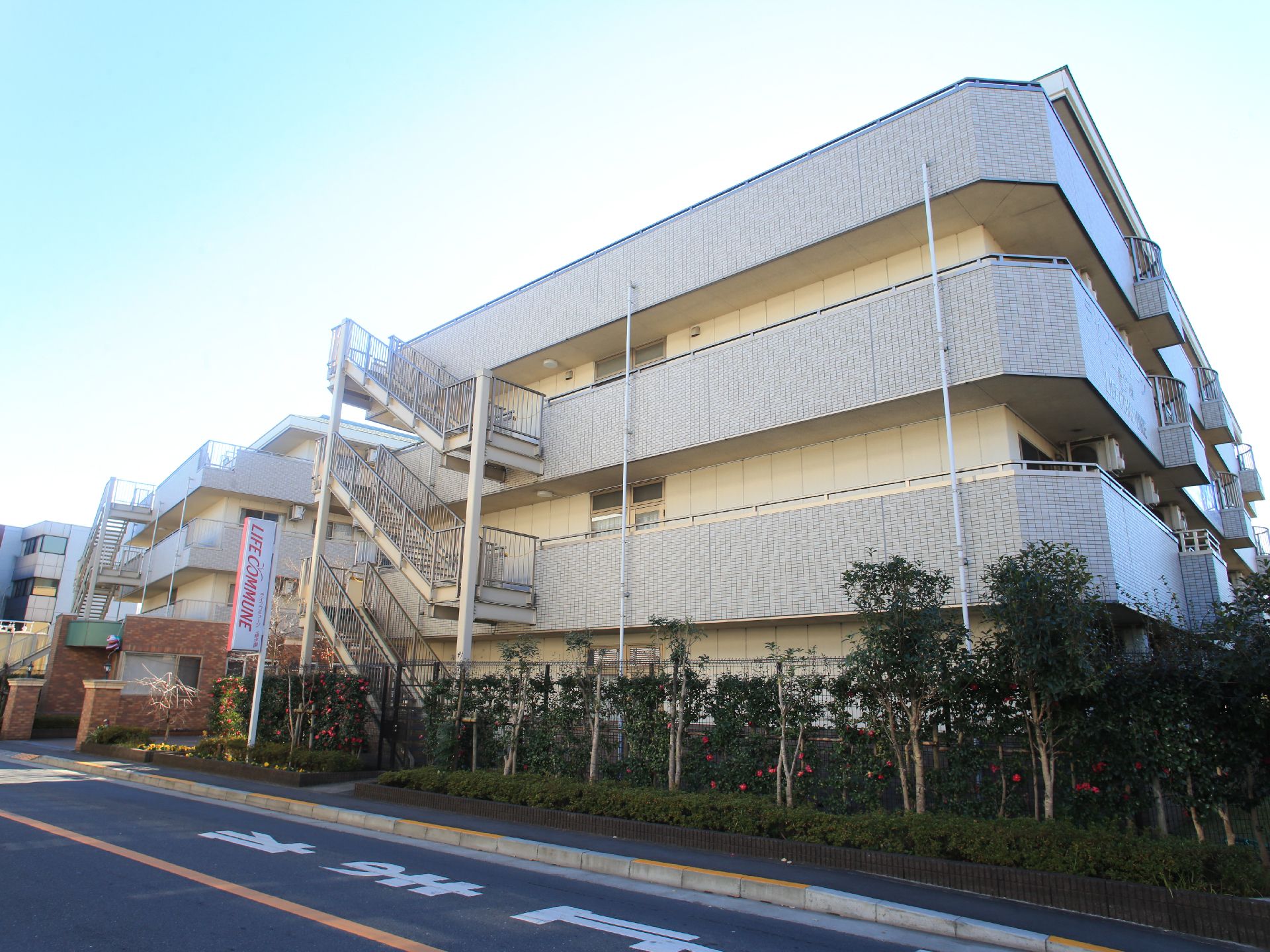 柵に隣接して植えられた緑に囲まれた、三階建ての施設外観
