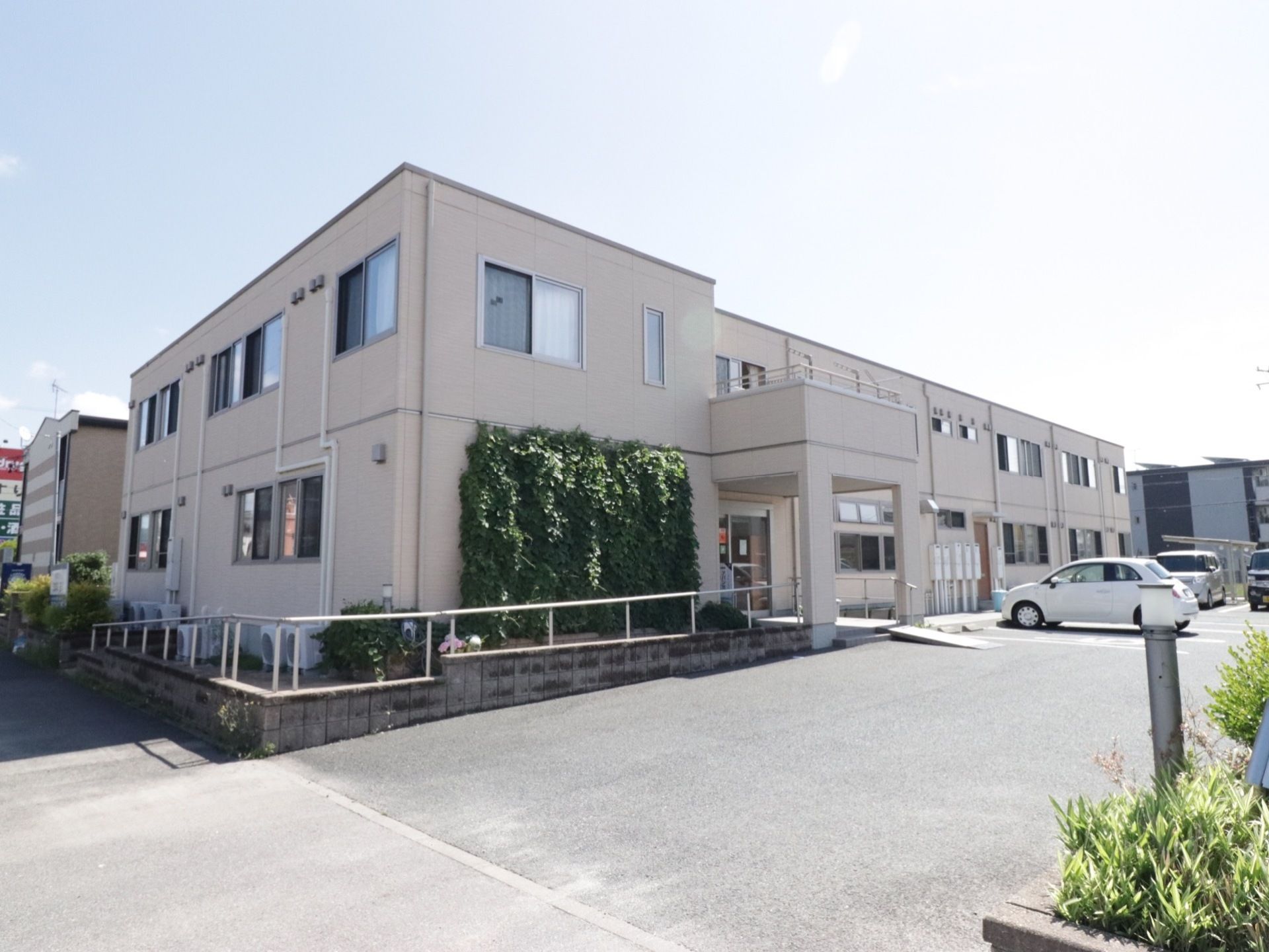 施設は、白で統一されたシンプルな外観となっている。正面には、広々とした駐車場スペースも設けられている。
