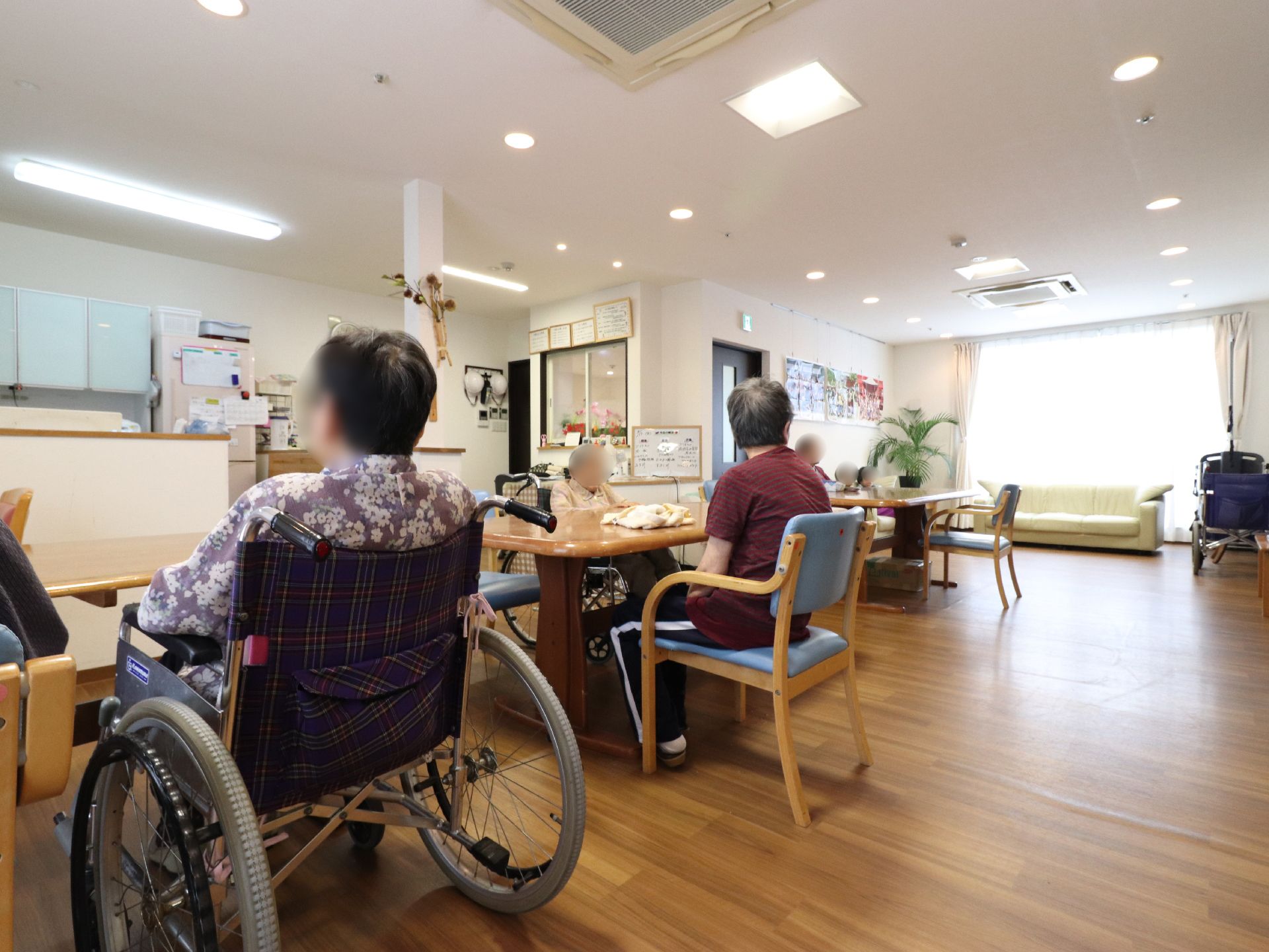 椅子に腰かけて食事をする食堂は、車イス利用者様でも利用することができる。天井まである掃き出し窓から光が入っている。