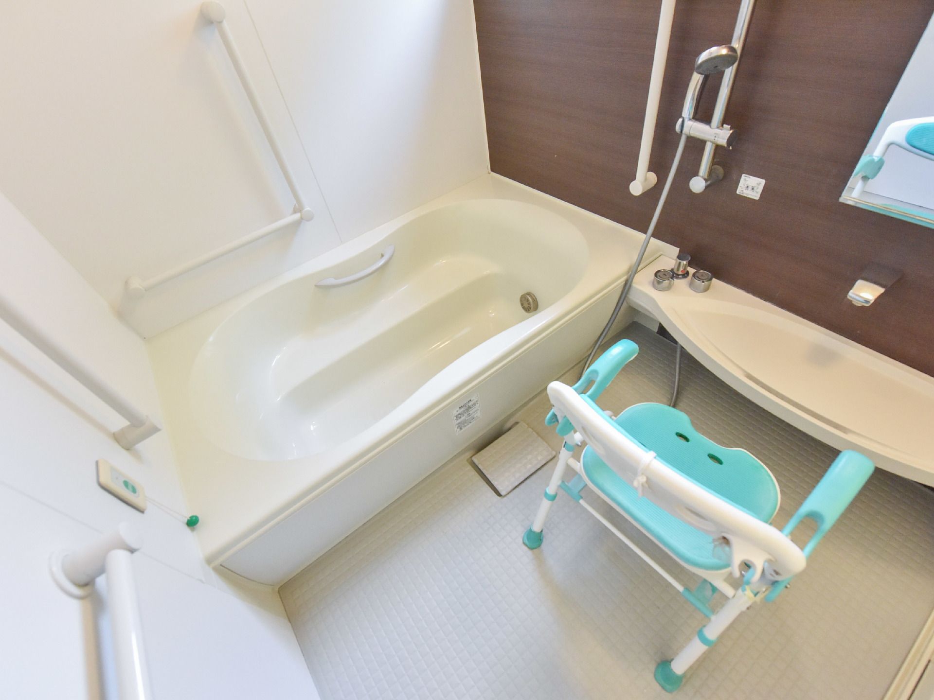 広々としたスペースの洗い場と手すりが取り付けられた浴槽が設置されている浴室。シャワーベンチも置かれている。