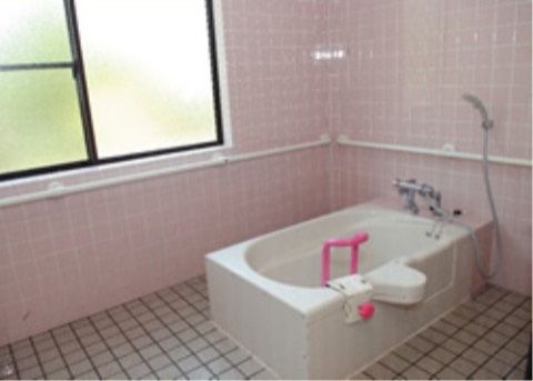 窓や入浴補助器具が設置された白いユニットバスが完備されている。壁には手すりが取り付けられ、安全対策がとられている。