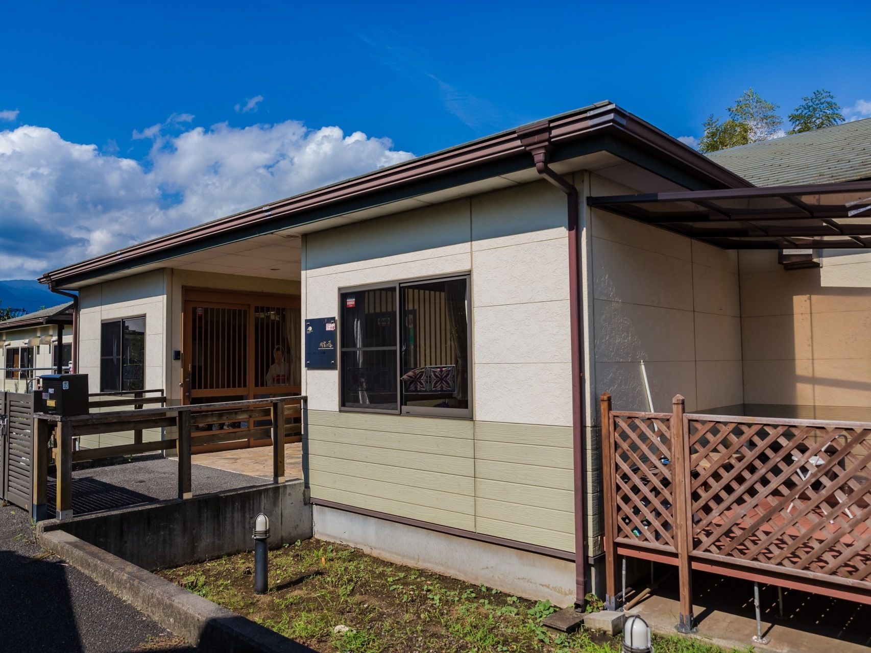 白を基調とした落ち着いた色合いの建物である。外壁には表札が取りつけられており、玄関前の門の横にはポストが設置されている。