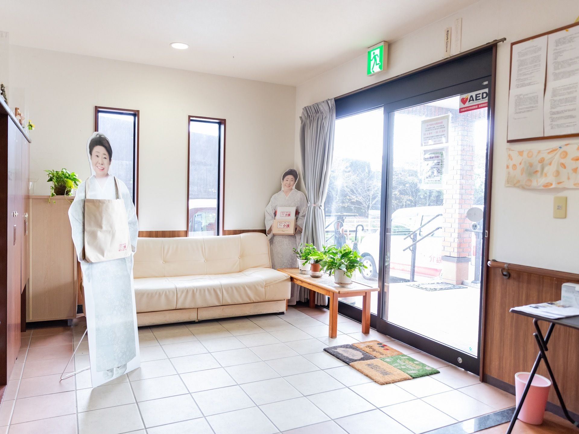 段差のない玄関の内部である。３人掛けの白いソファが置かれ、その前には芸能人の等身大パネルが置かれている。