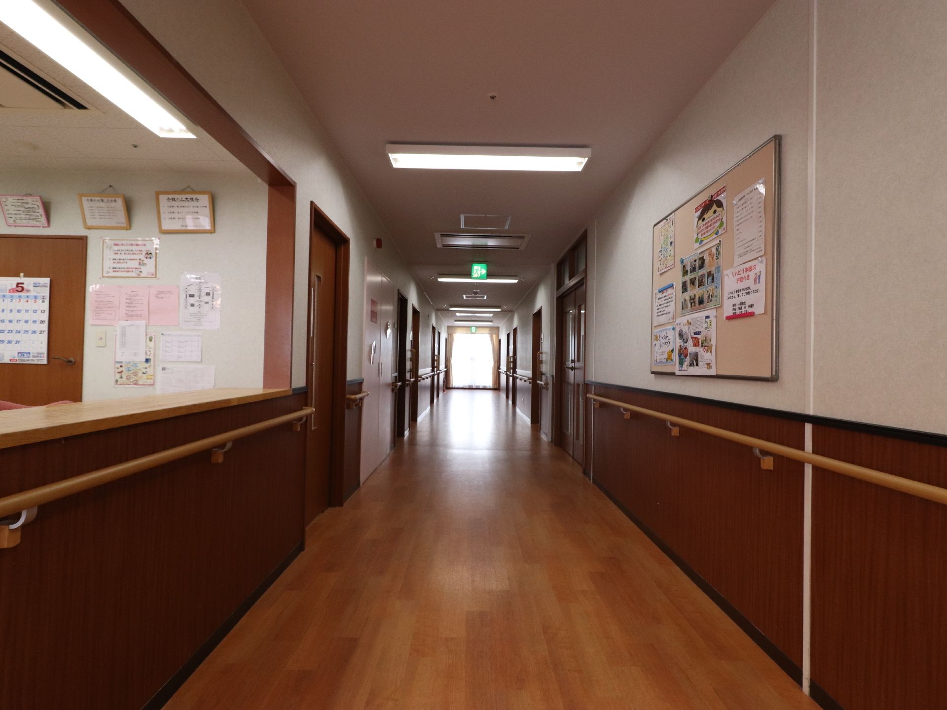 木目調の落ち着いた雰囲気の共用廊下になっている。手前には受付があり、その横に各居室が設けられている。