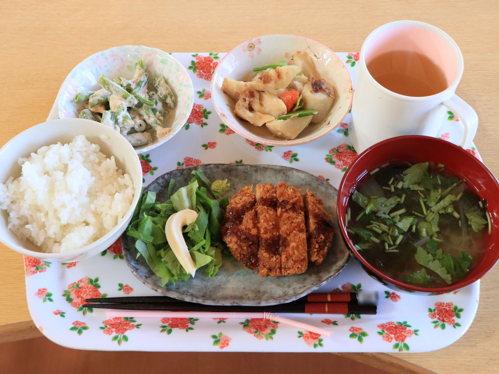 ある日の一汁三菜のメニューである。花柄のプレートに器に盛られて、飲み物とお箸と一緒に並べられている。