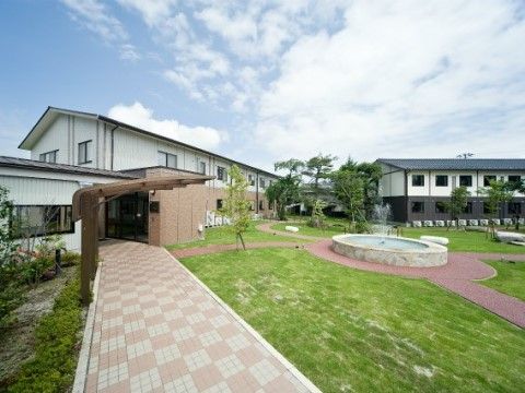芝生の広場に噴水があり、そこから四方に遊歩道が伸びている。右手には白黒の建物、左手には白と茶色の建物がある。