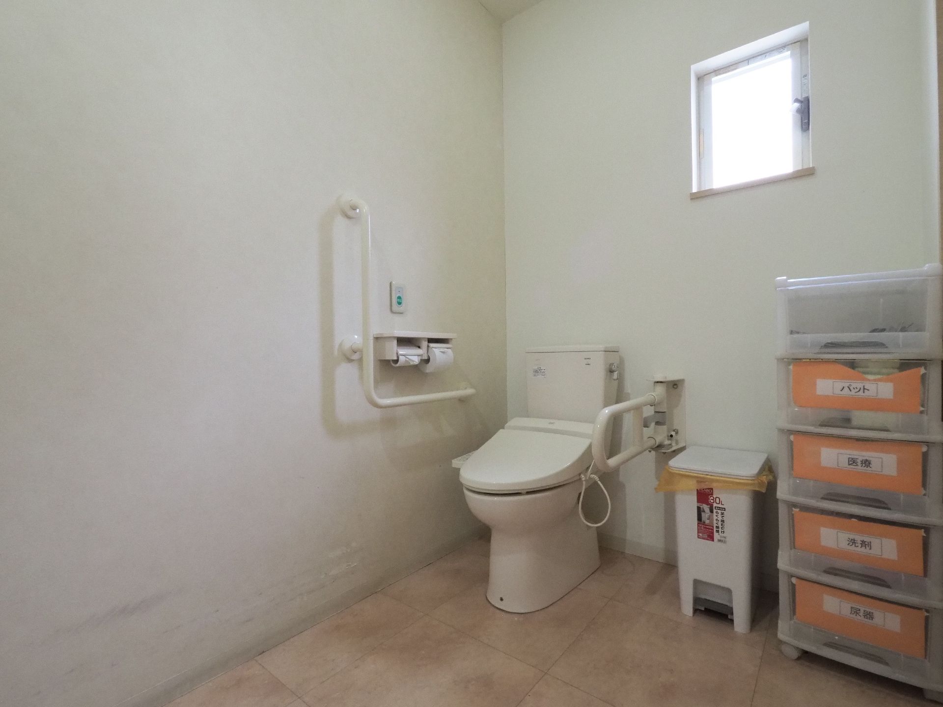 清潔感のあるトイレである。便器横には汚物用の箱も設置されており、その横には必要な備品が収納ケースに入れられている。