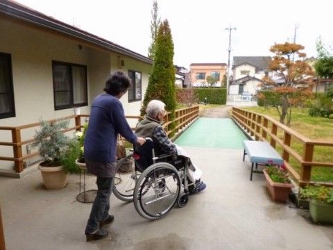 建物から車椅子をご利用の方と女性スタッフが出てきている。両側に柵があるスロープを降りようとしている。