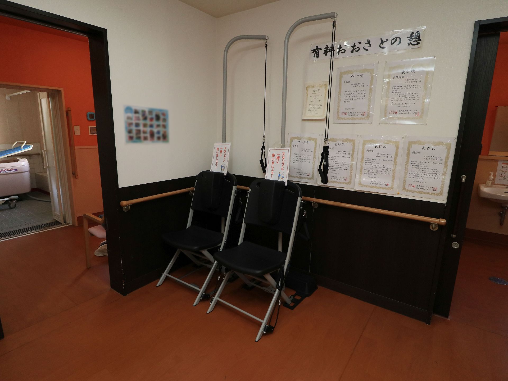 廊下の壁の上の方に施設名称が掲示され、その下に、施設が受けた感謝状が何枚も飾られている。奥には介護浴室が見える。