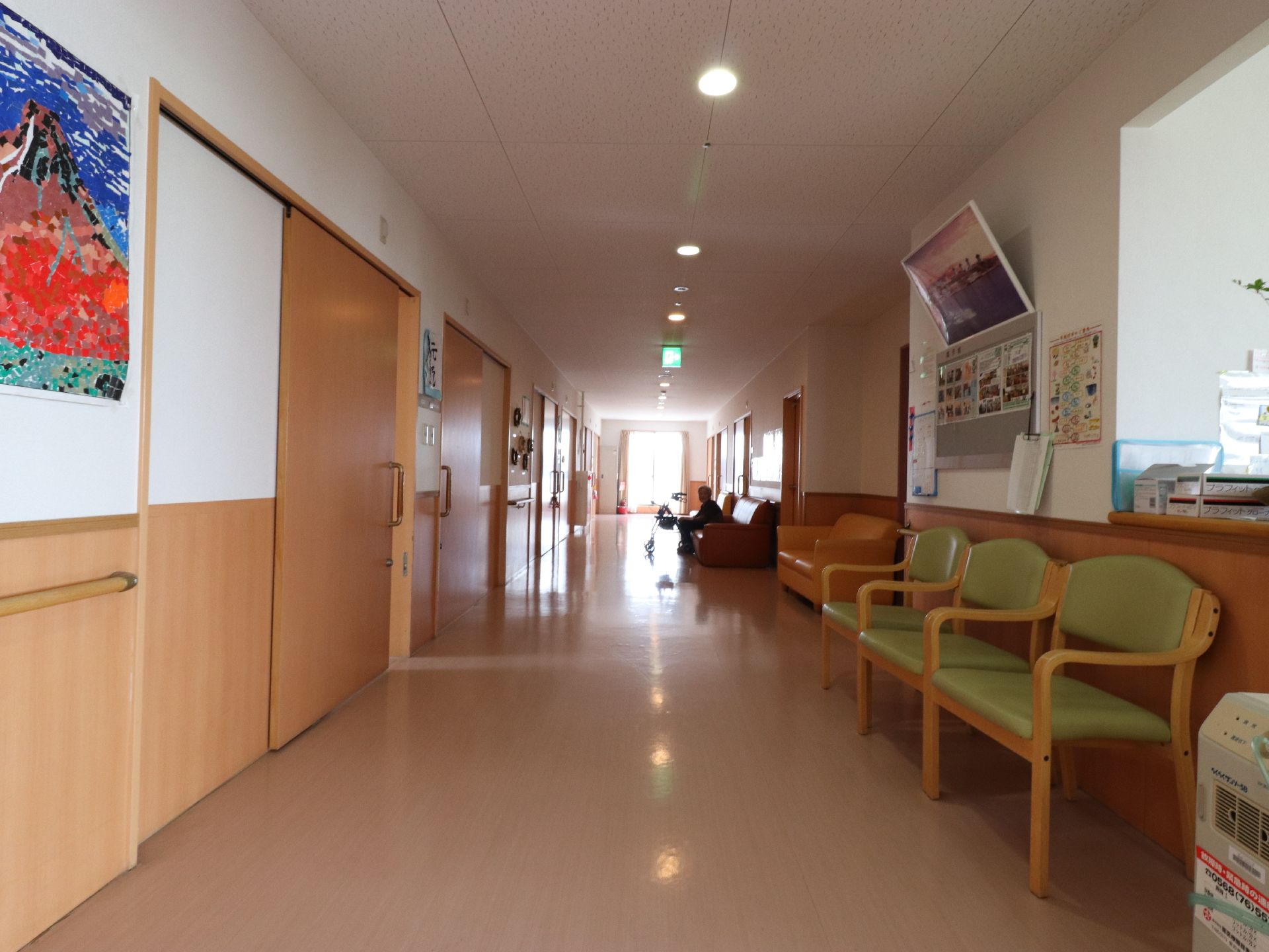 居室間を結ぶ廊下はフローリングになっている。椅子やソファーが置かれており、壁には手すりがついている。