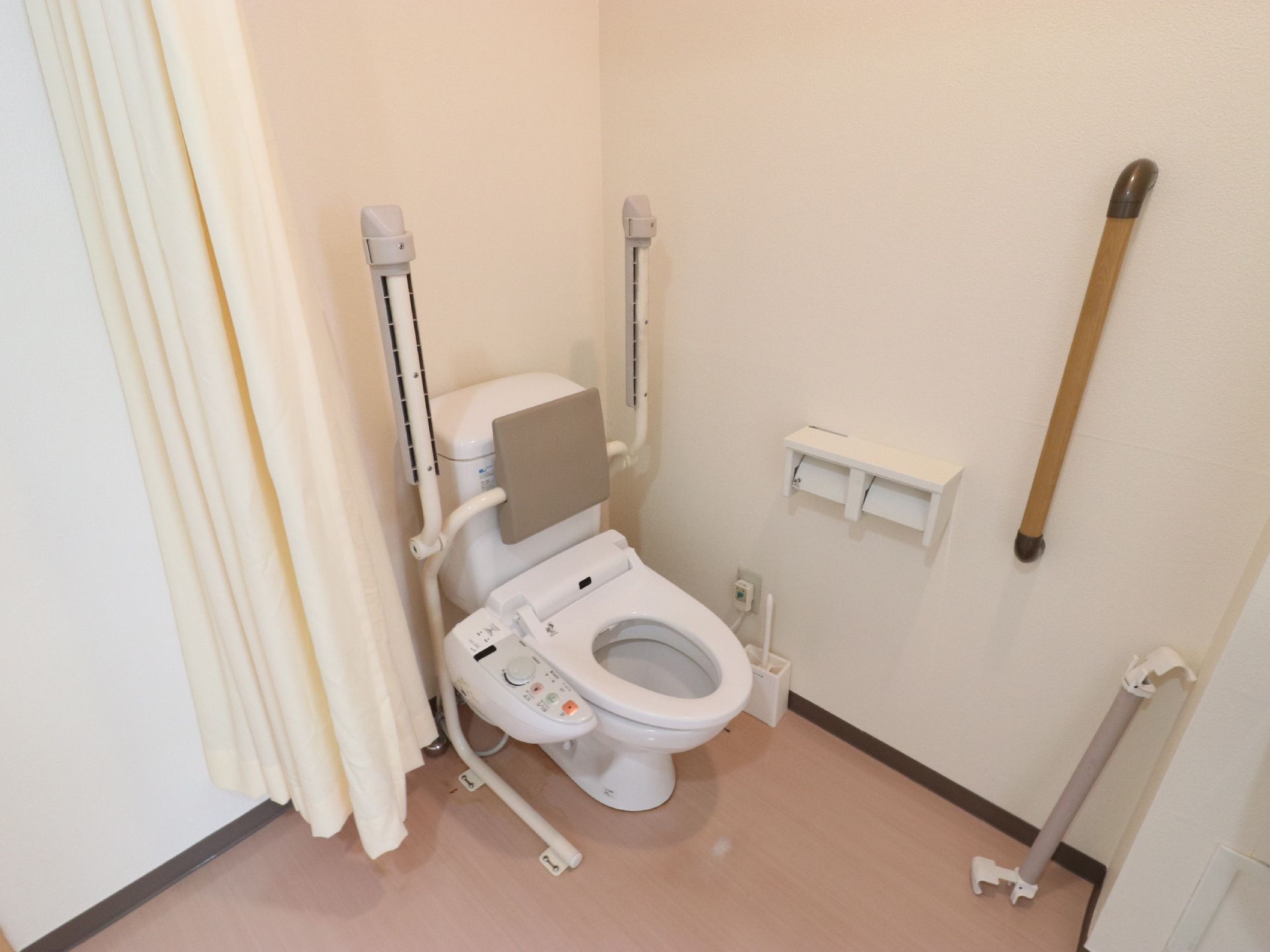 トイレはウォッシュレットで、手元で操作ができる。背もたれと手すりがついていて、手すりは動かすことが可能。