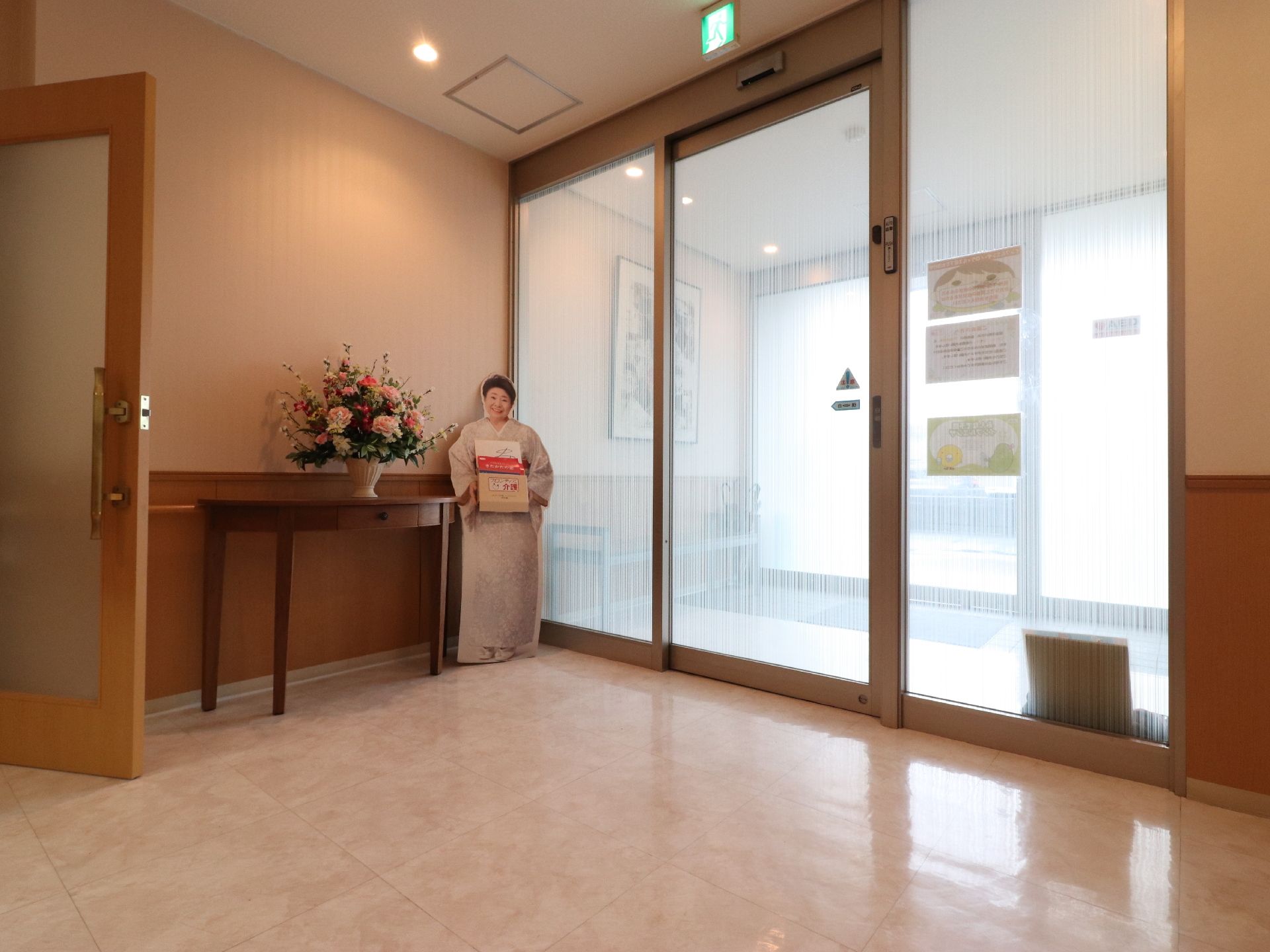 玄関から施設内に入るドアは自動になっているので、車イスの方も安心である。傘置場が設置されていて、その上には絵が飾られている。